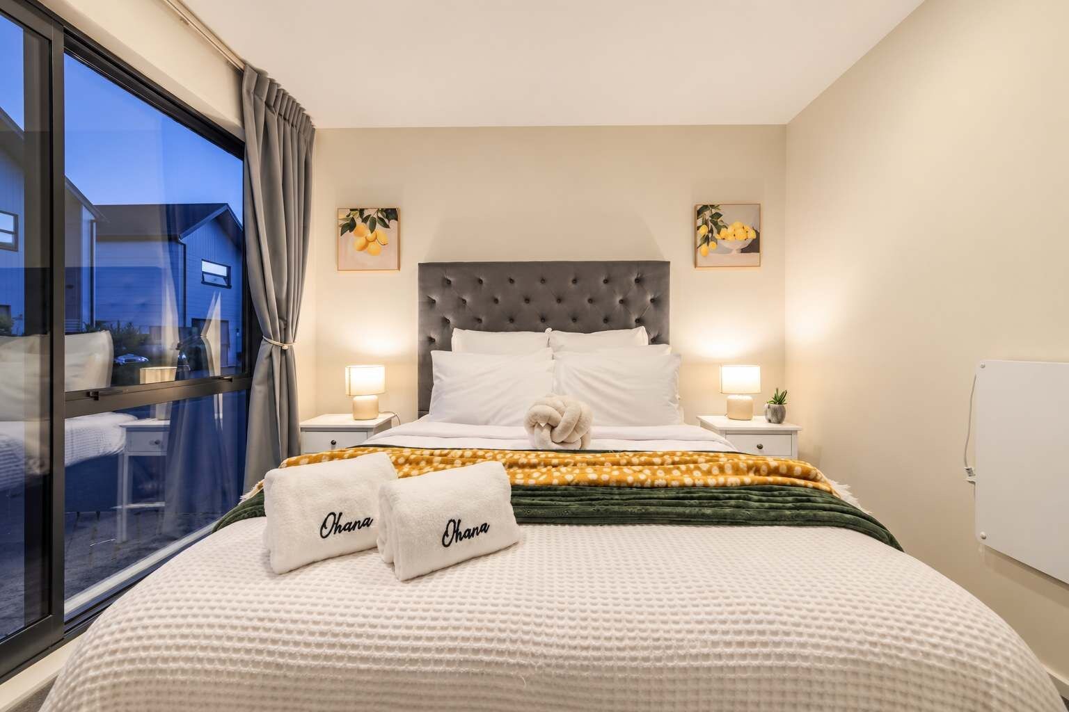 Ett hotellrum med en stor säng, två sänglampor, ett fönster med gardiner och konstverk på väggarna.