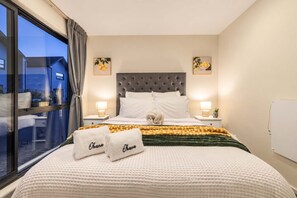 Habitación de hotel con una cama grande, dos lámparas de noche, una ventana con cortinas y obras de arte en las paredes.