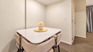 A room with a dining table, four chairs, a vase with flowers, and a door leading to another room.