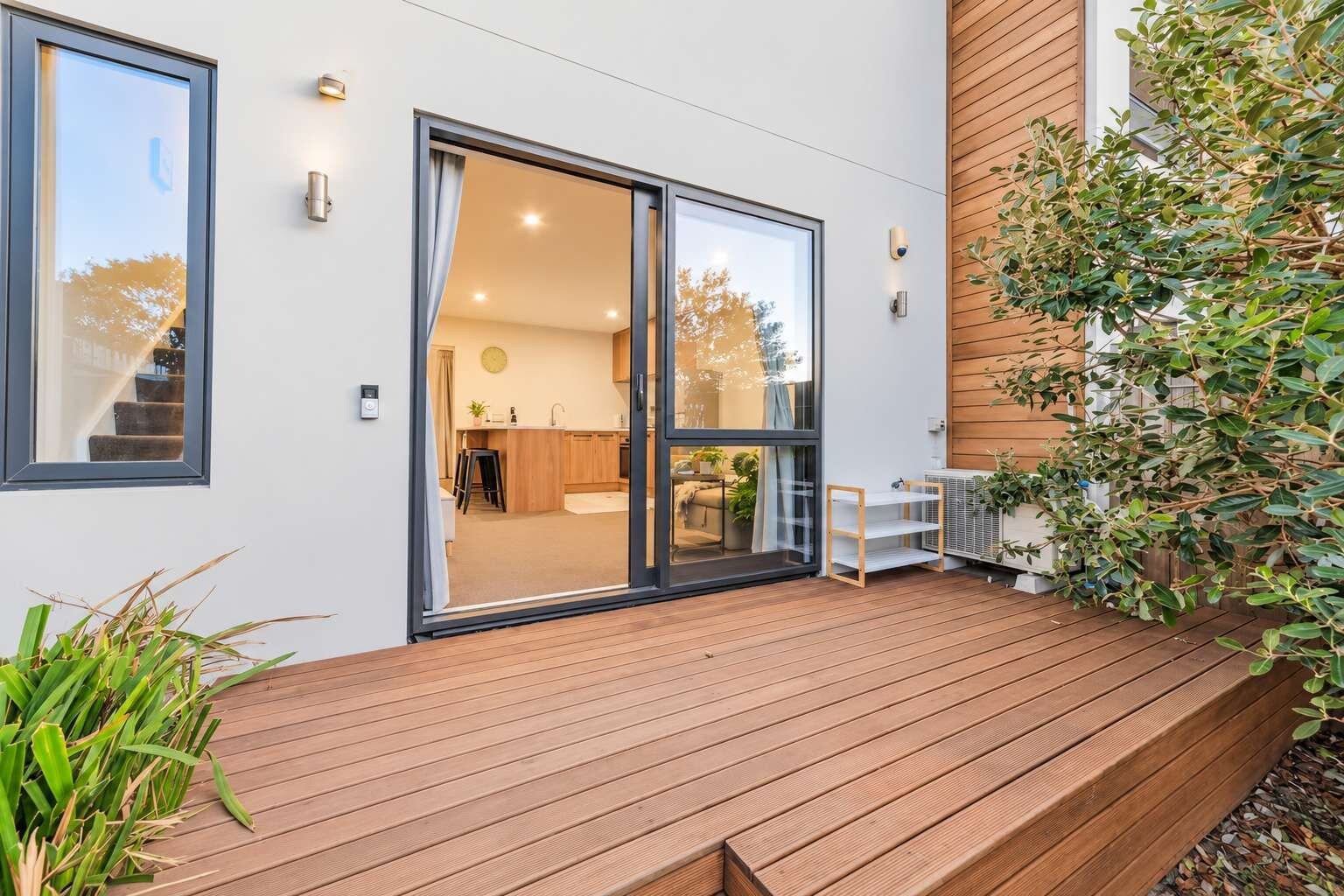 A modern house with a wooden deck, a sliding glass door leading to a kitchen, and a small outdoor seating area.