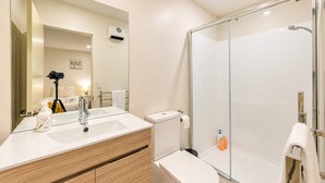 A modern bathroom with a glass shower enclosure, a vanity with a mirror, and a camera on a tripod.