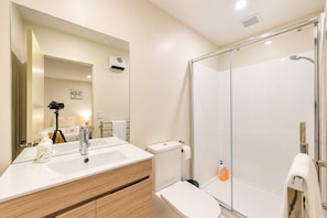 A modern bathroom with a glass shower enclosure, a vanity with a mirror, and a camera on a tripod.