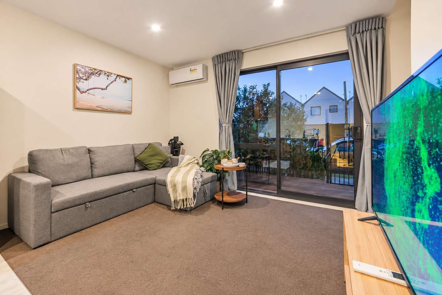 A modern living room with a grey sectional sofa, a small side table with a plant, and a large window with curtains.