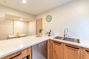 Una cocina moderna con encimera blanca, armarios de madera, un lavamanos de acero inoxidable y un reloj de pared.