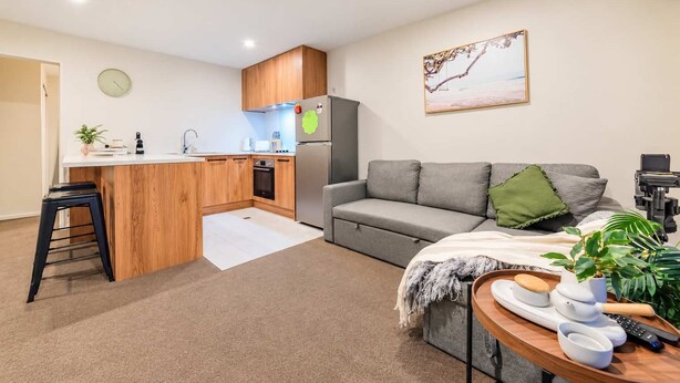 A compact living space with a kitchenette, a grey sofa, a small dining table, and a single chair.