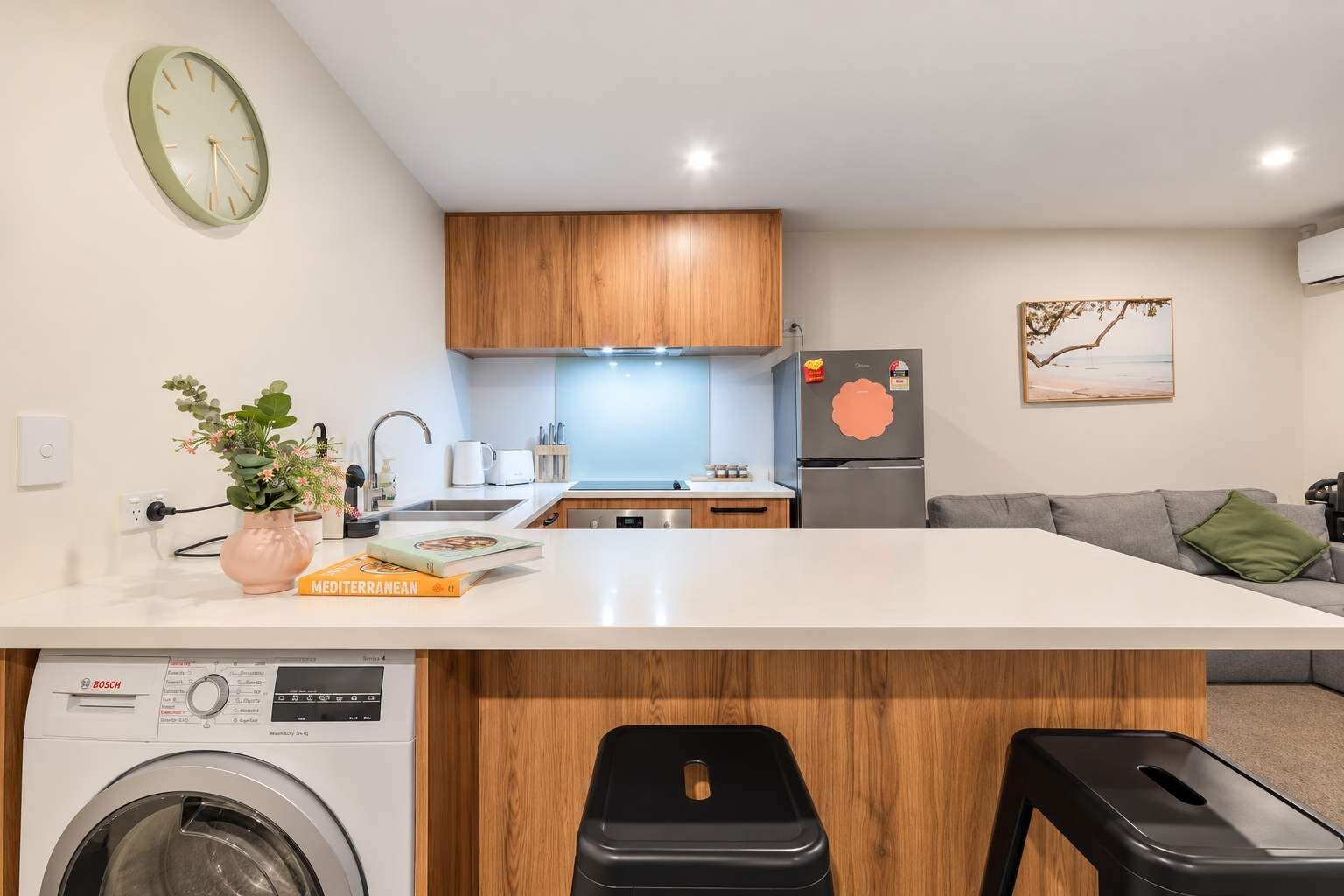 A modern kitchen with wooden cabinets, a built-in washing machine, and a large island with bar stools.