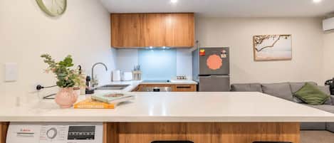 A modern kitchen with wooden cabinets, a built-in washing machine, and a large island with bar stools.