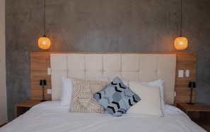 Una cama con cabecera capitonada, dos lámparas de noche y almohadas estampadas.