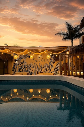 Un área de piscina con un mural tropical, luces colgantes y una palmera.