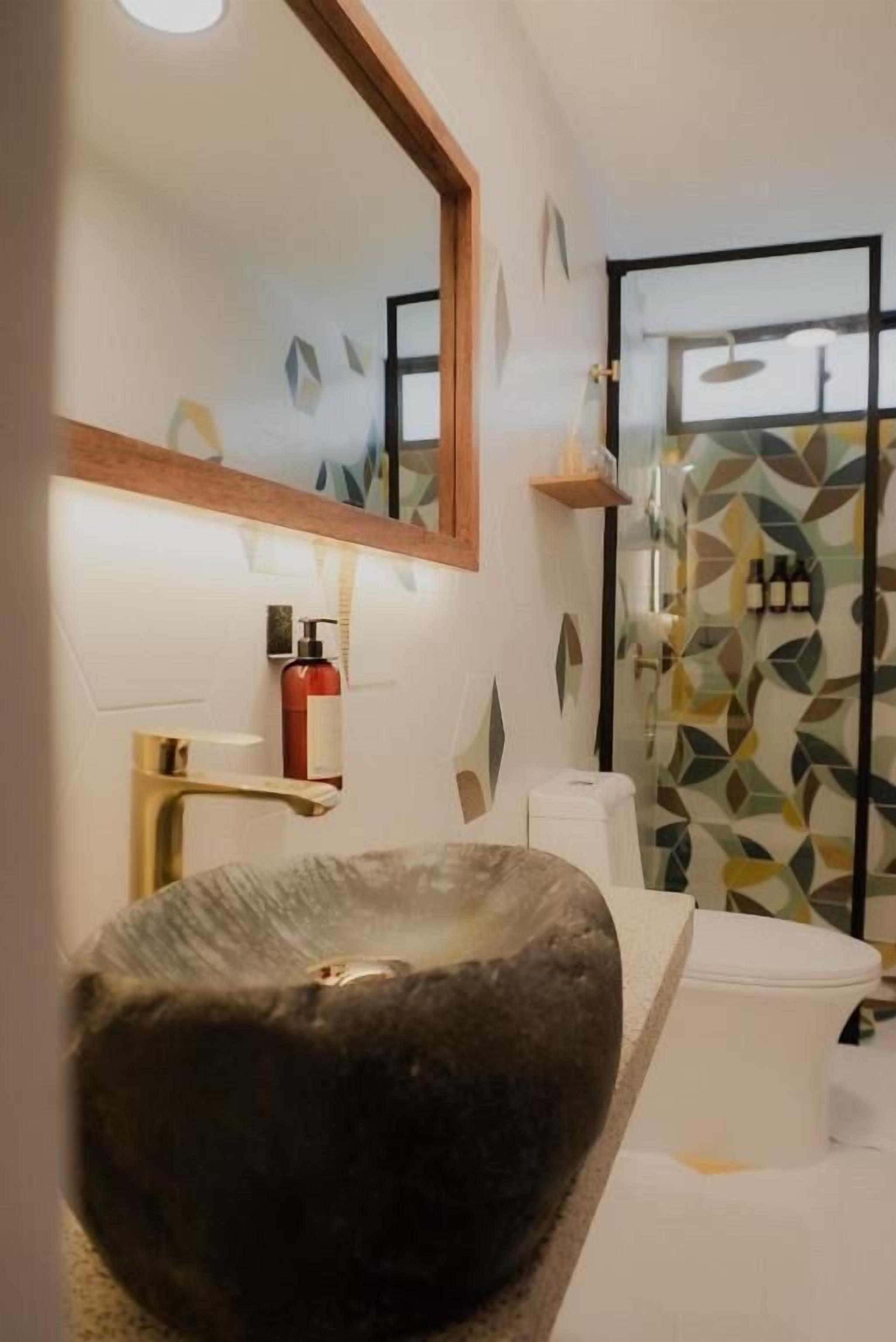 A bathroom with a stone basin, a mirror, a towel rack, and a shower area.