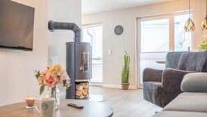 A modern living room with a wood-burning stove, a sofa, a coffee table, and a TV mounted on the wall. - Stunning apartment in Kappeln with sauna (Kappeln)