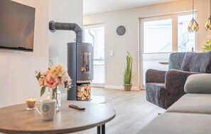 Ein modernes Wohnzimmer mit Kaminofen, einer Couch, einem Couchtisch und einem an der Wand befestigten Fernseher.