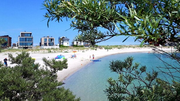 A beach with modern buildings in the background, clear blue water, and people enjoying the beach. - Stunning apartment in Kappeln with sauna (Kappeln)