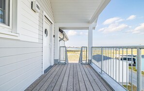 Ein weißes Gebäude mit einer überdachten Veranda und Blick auf den Strand, sowie ein dort abgestellter Wohnmobilwagen.