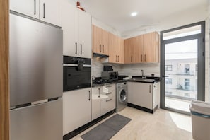 A modern kitchen with stainless steel appliances, wooden cabinets, and a large window. - Luxury apartment, Agadir bay, pool&fibre (Agadir)