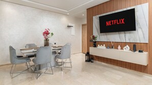 A modern living room with a dining area, a flat-screen TV mounted on a wooden wall, and a minimalist console table. - Luxury apartment, Agadir bay, pool&fibre (Agadir)