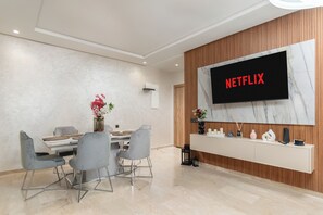 A modern living room with a dining area, a flat-screen TV mounted on a wooden wall, and a minimalist console table. - Luxury apartment, Agadir bay, pool&fibre (Agadir)