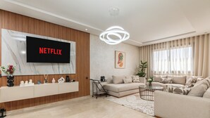 A modern living room with a large flat-screen TV, a sofa, a coffee table, and a decorative plant. - Luxury apartment, Agadir bay, pool&fibre (Agadir)