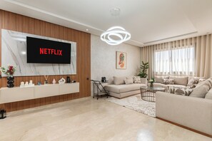 A modern living room with a large flat-screen TV, a sofa, a coffee table, and a decorative plant. - Luxury apartment, Agadir bay, pool&fibre (Agadir)