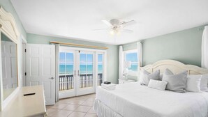 Une chambre à coucher comprenant un lit, une table de chevet, un ventilateur de plafond, une porte et une vue sur l’océan, visible à travers une porte coulissante.