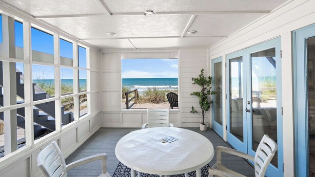 Un espace extérieur abrité, doté d’une table et de chaises, offrant une vue sur la plage et comprenant un escalier menant à la plage.