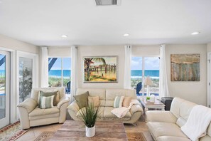 A living room with a beige sofa, a coffee table, and a potted plant. There are large windows with a view of the beach. - Ocean Front Home, Gorgeous Views, Beach Gear, BBQ (St. Augustine)