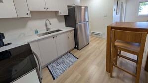 Une cuisine moderne avec des meubles blancs, un réfrigérateur en acier inoxydable, une table à manger en bois et un plan de travail noir.