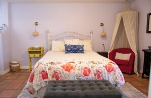 Ein Schlafzimmer mit Bett, Nachttischen, einer Bank, einem roten Sessel und einem Baldachin.