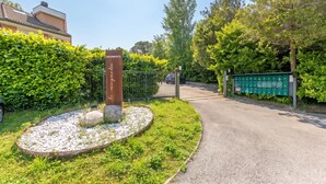 Ein verschlossenes Tor mit einem Schild, ein Kiesweg und ein Heckenstreifen.