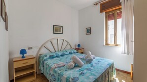 Un dormitorio con una cama, una mesita de noche, una ventana con cortinas y un estante fijado a la pared.