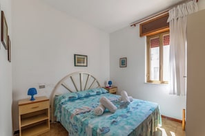 Ein Schlafzimmer mit einem Bett, einem Nachttisch, einem Fenster mit Vorhängen und einem an der Wand befestigten Regal.