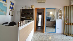 Una recepción con una placa de identificación, un ventilador de techo, un mapa en la pared y una puerta que da a una zona de cocina.