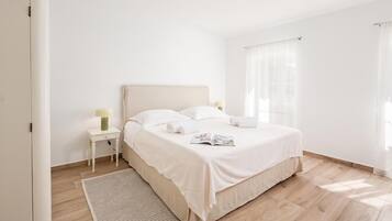 Un dormitorio minimalista con una cama individual, una mesita de noche con lámpara y una ventana con cortinas translúcidas.