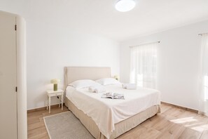 Un dormitorio minimalista con una cama individual, una mesita de noche con lámpara y una ventana con cortinas translúcidas.