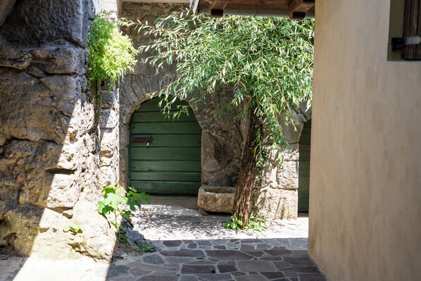 Un arco de piedra que da a una puerta verde, rodeado de muros de piedra y un pequeño árbol.