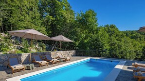 Una piscina amb gandules i ombrelles, envoltada per murs de pedra i arbres.