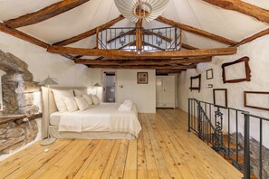 A bedroom with a wooden floor, a bed with white bedding, a stone wall, and a staircase with a wrought iron railing. - Nature & Pool Escape - Stone House, Zvoneća, Croatia (Zvoneća)
