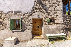 Un edificio de piedra con puerta de madera, una ventana verde y un banco afuera.