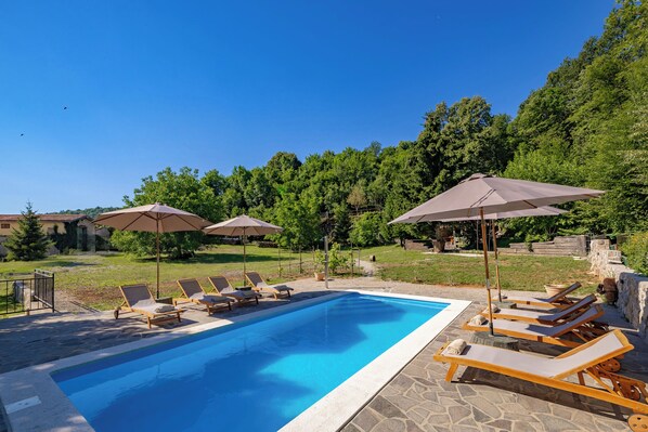 A swimming pool with lounge chairs and umbrellas, surrounded by a stone deck and greenery. - Nature & Pool Escape - Stone House, Zvoneća, Croatia (Zvoneća)