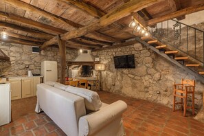 Un intérieur rustique avec des poutres apparentes, un mur en pierre, un canapé, une table à manger et un escalier.