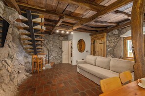 Et rustikt interiør med stenvæg, ​​trætrappe, sofa og spisebord.