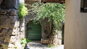 Un arc en pierre mène à une porte verte, qui est elle-même entourée de murs de pierre et d’un petit arbre.
