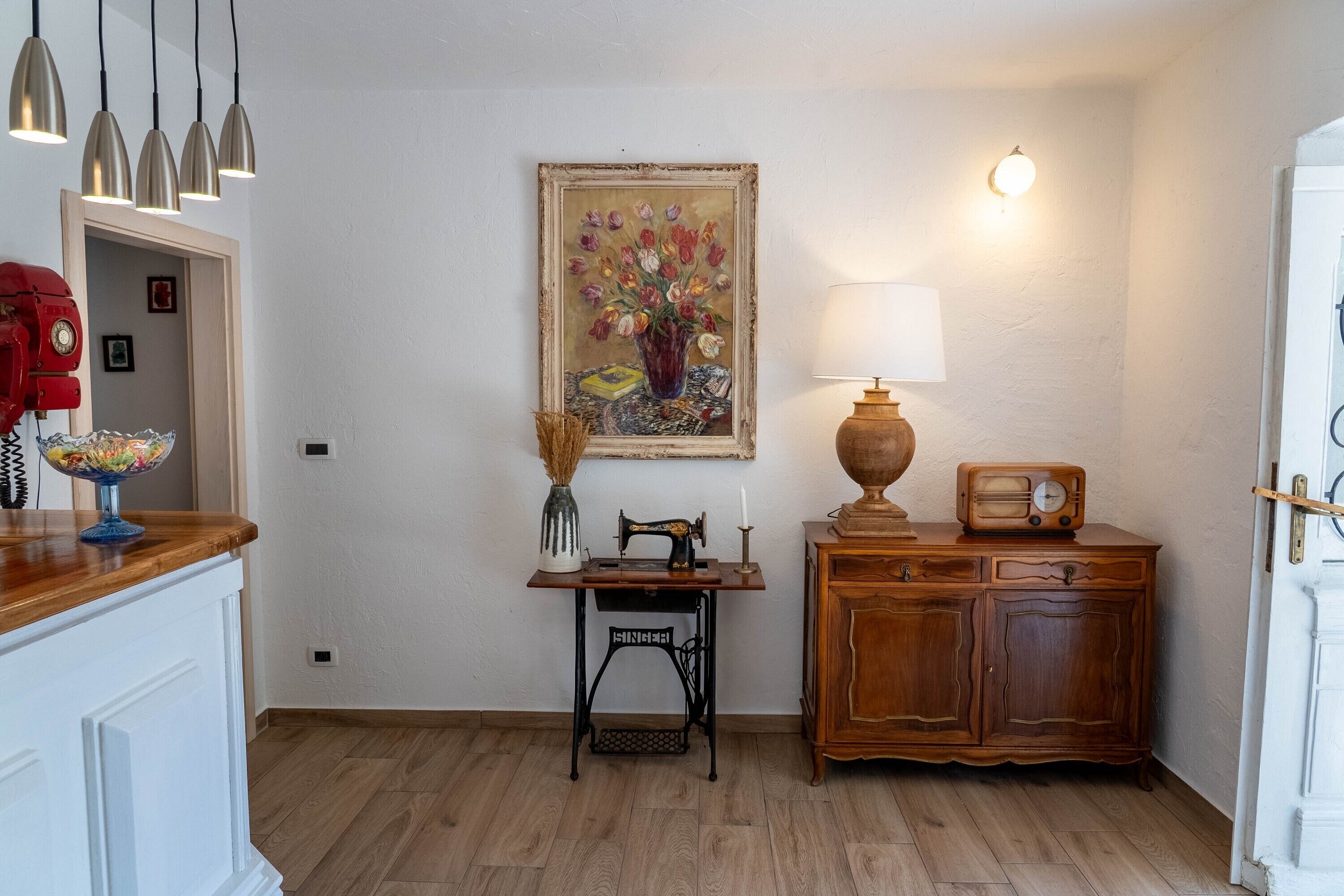 A room with a sewing machine, a lamp, a radio, and a painting on the wall.