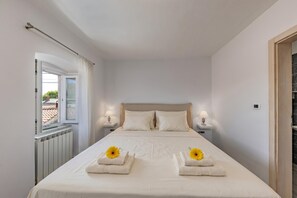 Ett hotellrum med en säng, två sängbord med lampor, ett fönster med gardiner och ett element.