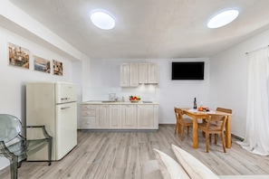 Una cocina compacta con refrigerador, armarios de madera, una mesa de comedor con sillas y un televisor de pantalla plana montado en la pared.