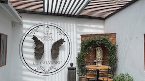 A patio area with a round table, chairs, a decorative wall with a logo, and hanging lights. - HOTEL CUADRA CASONA EL CALVARIO (Huichapan)