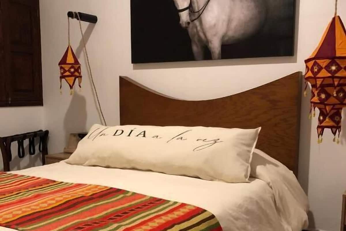 Una cama con cabecera blanca, una manta con rayas de colores y un almohadón con texto.