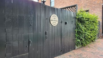 Een zwart houten hek met een rond bord, een gebouw van baksteen en een haag op de achtergrond.