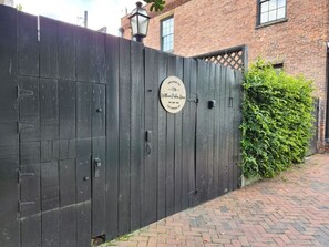 A black wooden gate with a circular sign, brick building, and a hedge in the background. - William Parker House - Garden Level on Warren Square (Savannah)
