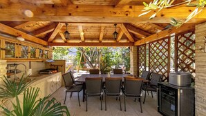 Eine Holzbalkendecke, eine Küche mit Schränken und Spüle, ein Essbereich mit Tisch und Stühlen sowie ein Kühlschrank.